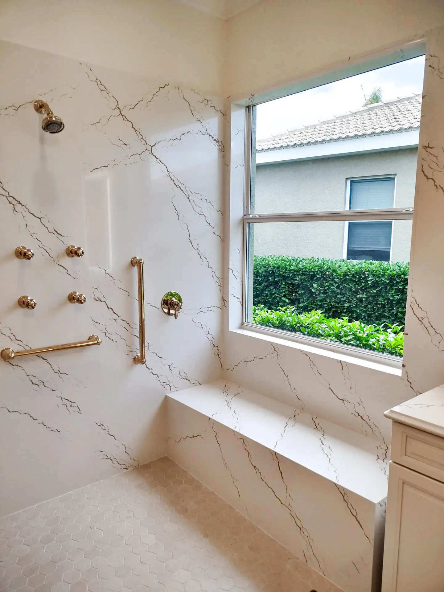 Modern master bathroom remodel in Venice, Florida featuring Cambria Inverness Gold quartz countertops and shower walls, sleek LED mirrors, and a large window letting in natural light.