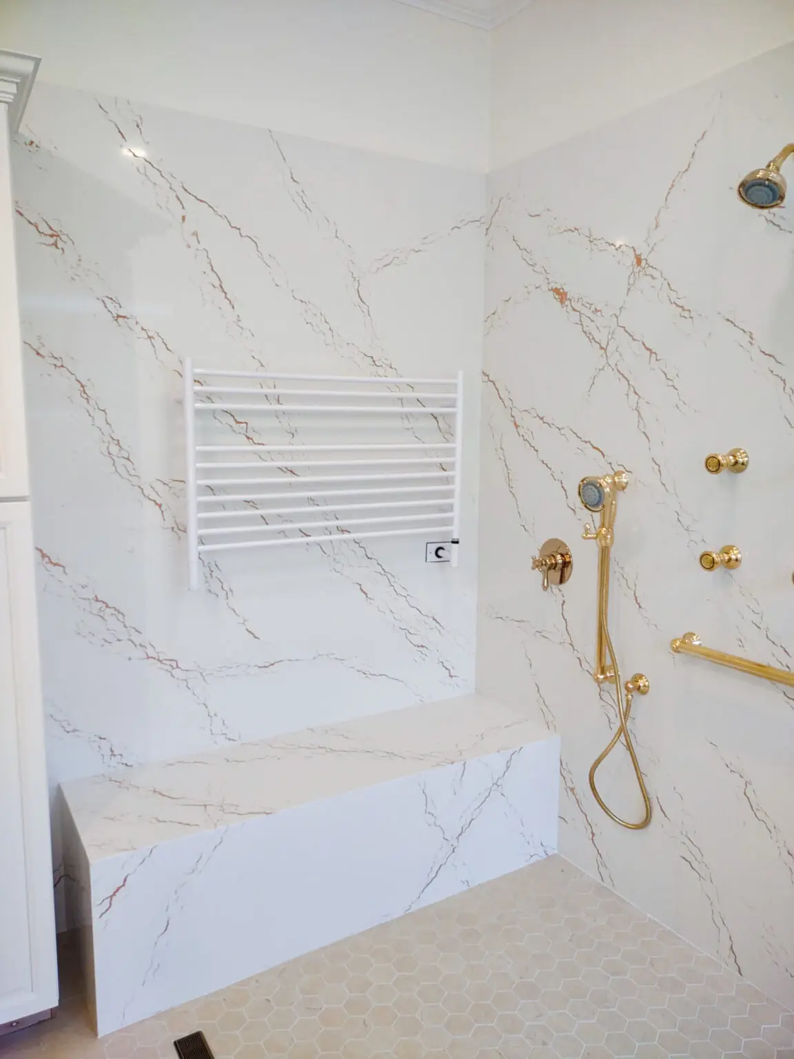 Angled view of shower walls in a Venice, Florida master bathroom remodel, featuring smooth Cambria Inverness Gold quartz surfaces that create a clean and elegant finish.