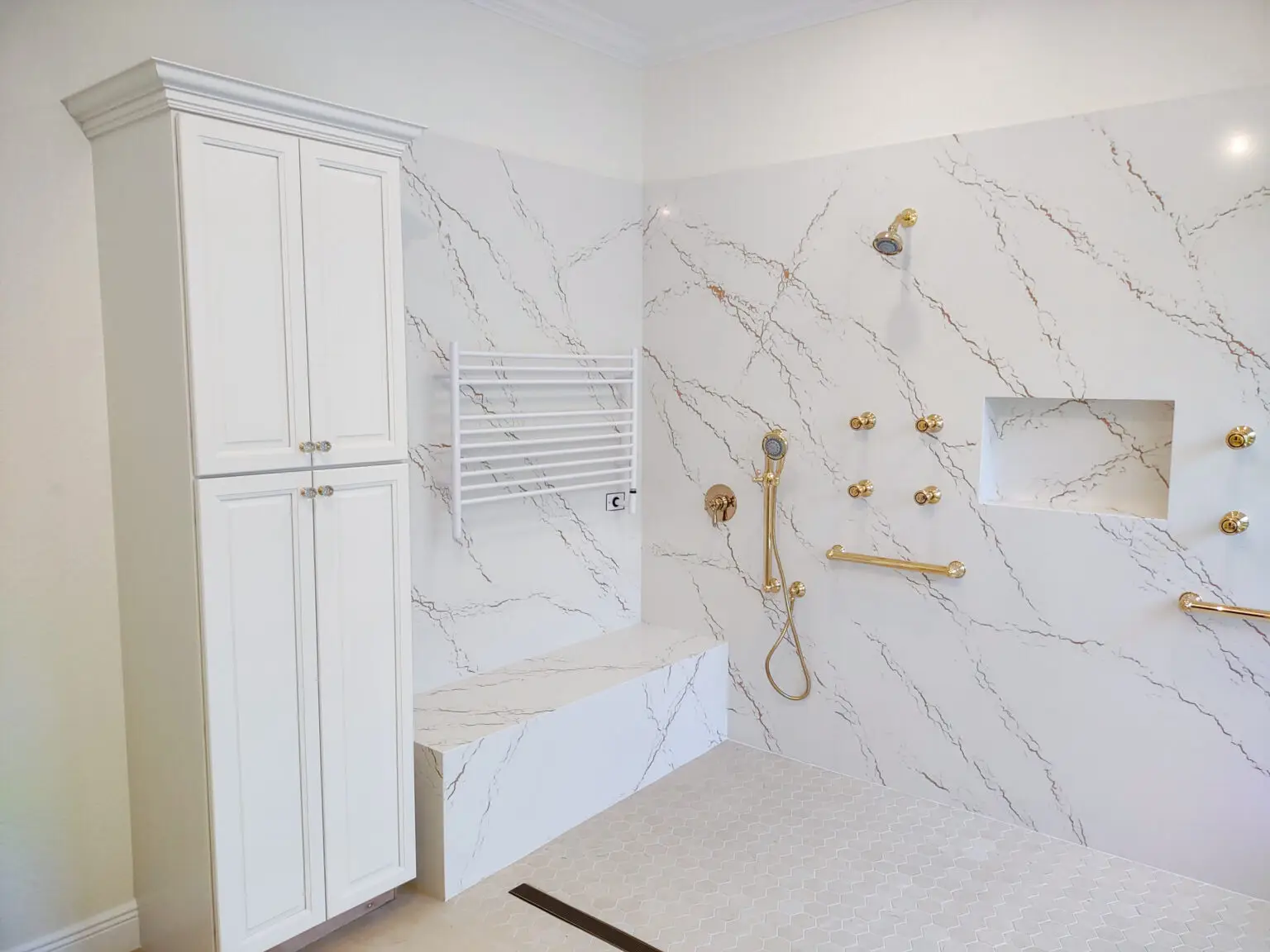 Angled view of shower walls in a Venice, Florida master bathroom remodel, featuring smooth Cambria Inverness Gold quartz surfaces that create a clean and elegant finish.